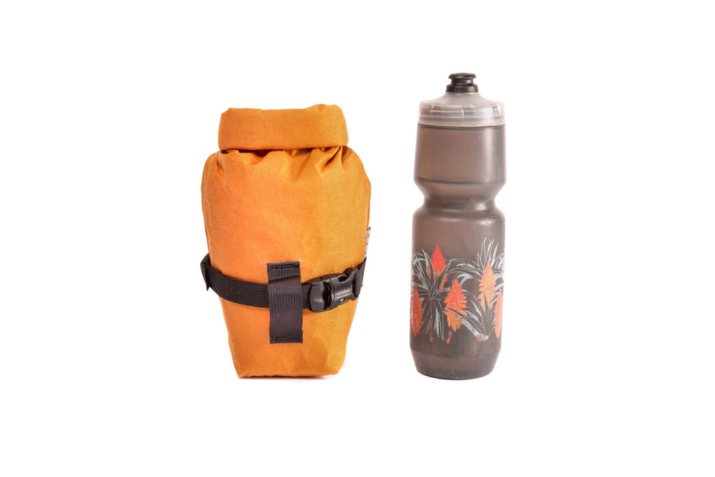 Outer Shell Rolltop Saddlebag, orange, next to a water bottle for scale