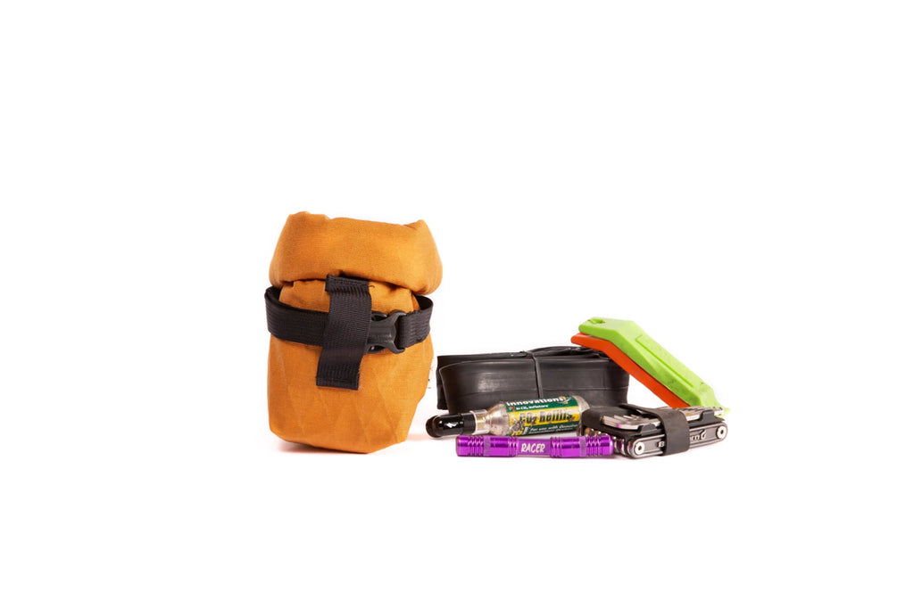 Outer Shell Rolltop Saddlebag, orange, next to the tools and snacks it holds