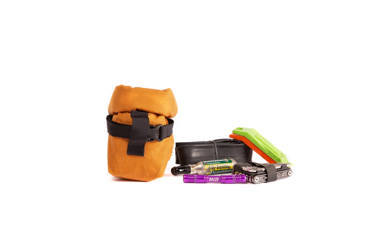 Outer Shell Rolltop Saddlebag, orange, next to the tools and snacks it holds