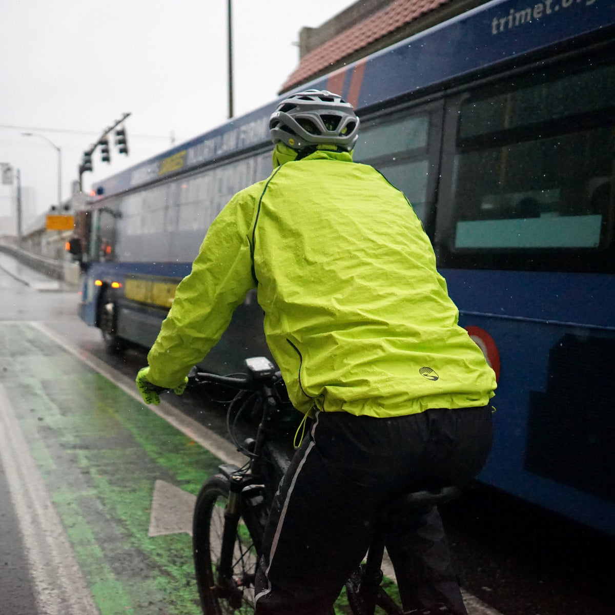 Men's Syncline CC Jacket, hi-vis yellow, rider seen from behind next to a bus