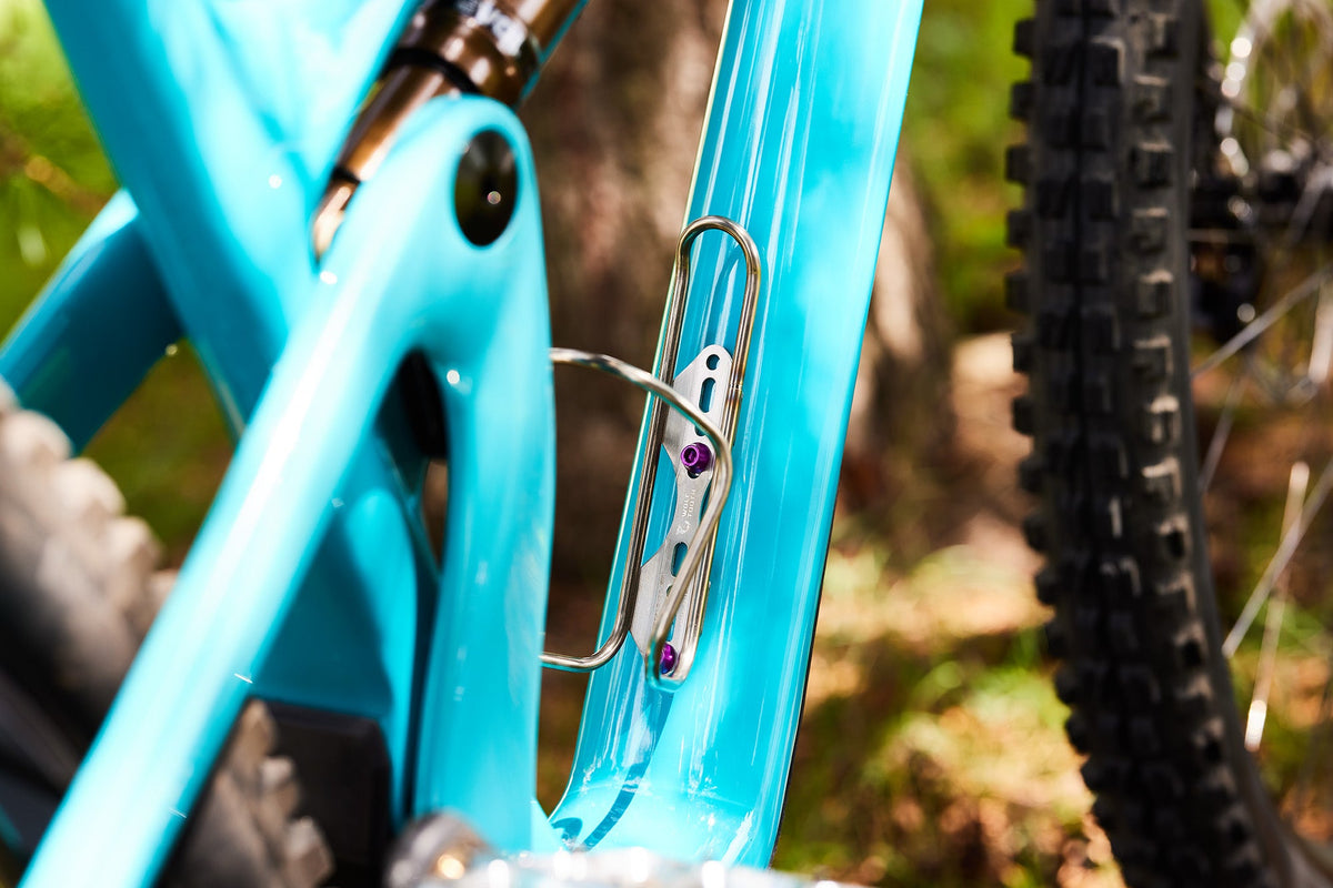 Wolf Tooth Morse Cage, Stainless Steel, mounted on a teal frame