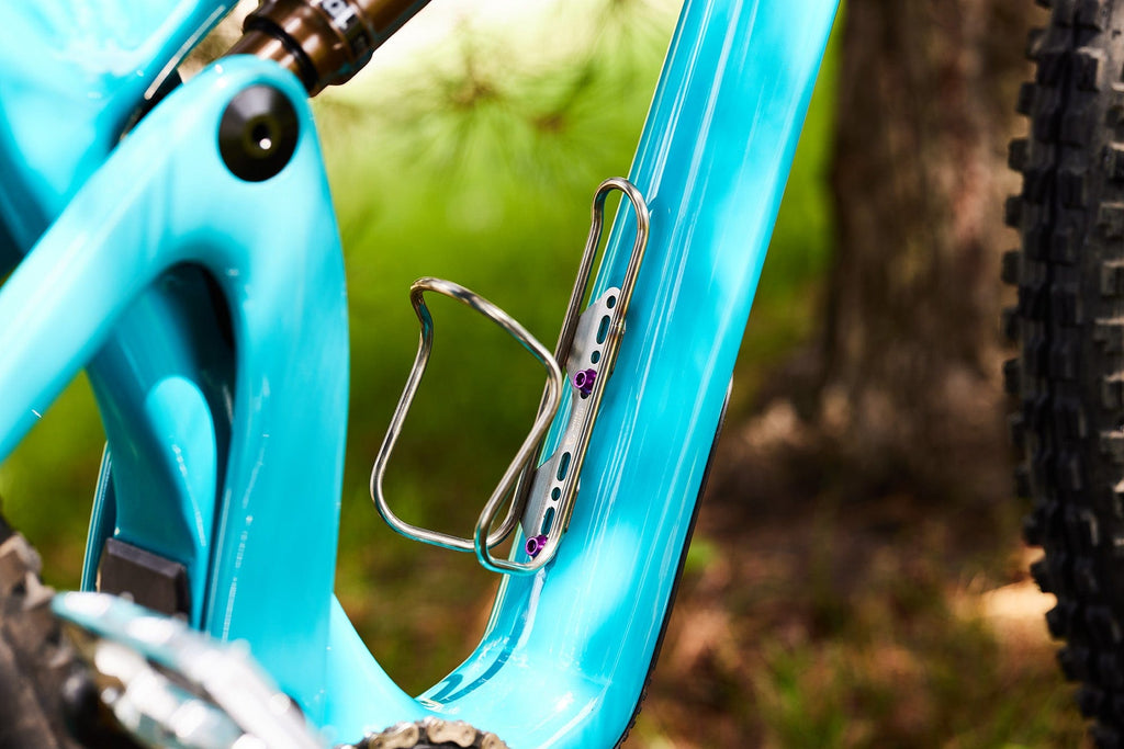 Wolf Tooth Morse Cage, Stainless Steel, mounted on a teal frame, wider view