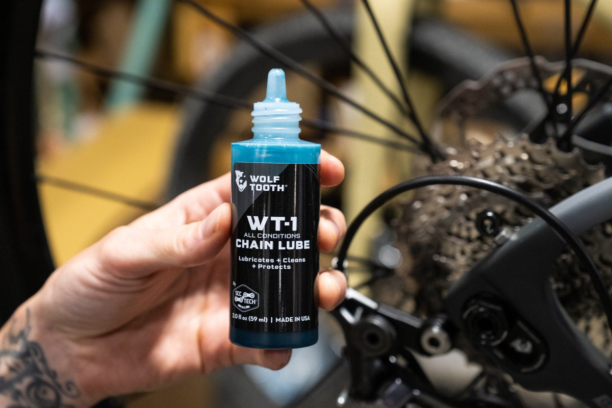 Wolf Tooth WT-1 Chain Lube, bottle held next to a cassette
