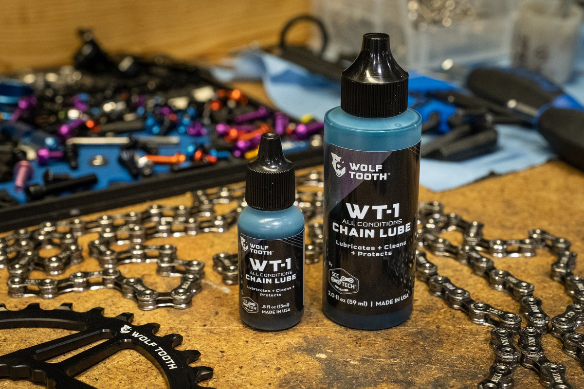 Wolf Tooth WT-1 Chain Lube, two bottle sizes on a workbench with chains