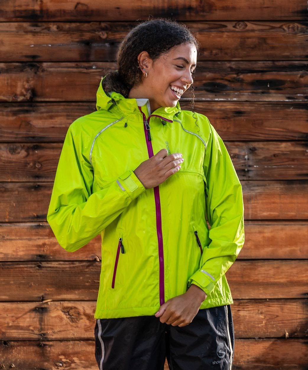 Women's Syncline CC Jacket, hi-vis yellow, worn standing in front of a wood wall