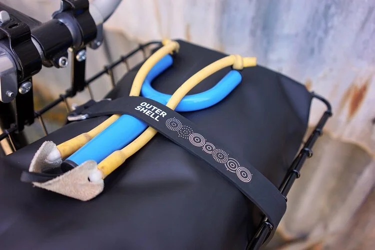 Outer Shell logo Voile strap in blue and yellow, holding tools against a black bag